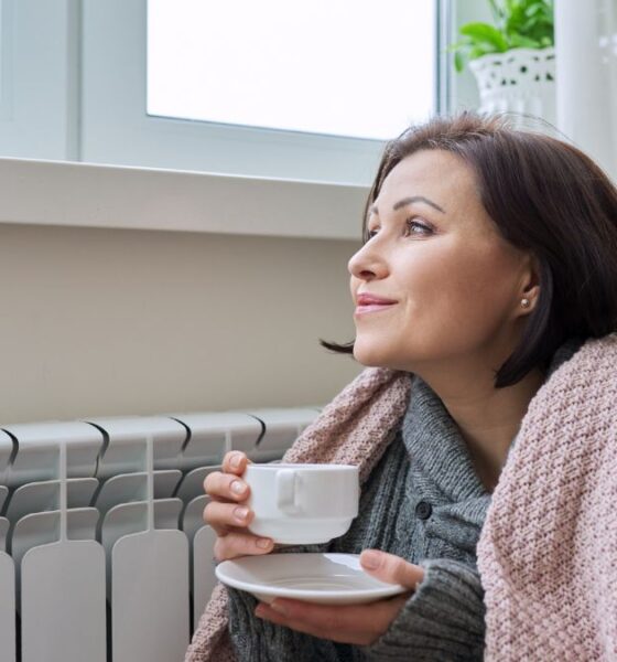 Žena pije čaj pored radijatora