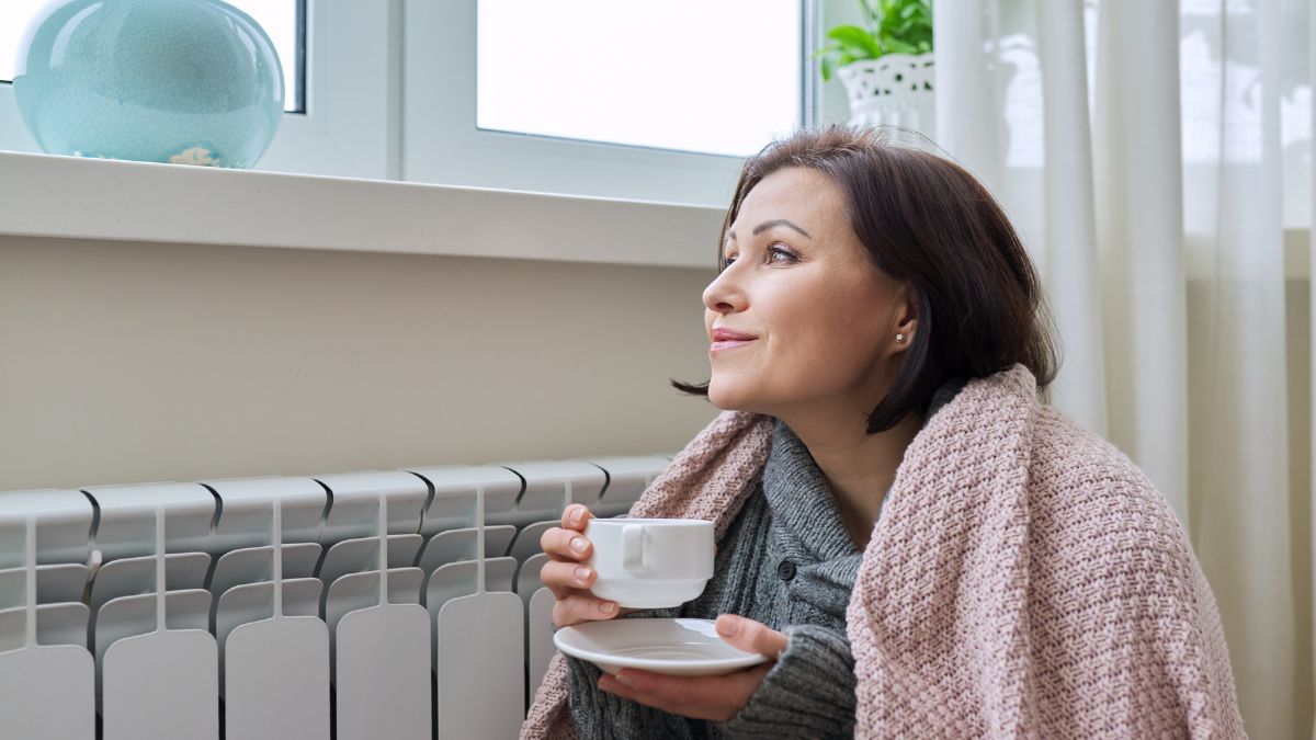 Žena pije čaj pored radijatora