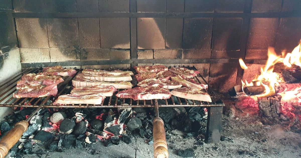Roštilj na drveni ugljen s mesom koje se peče iznad žara