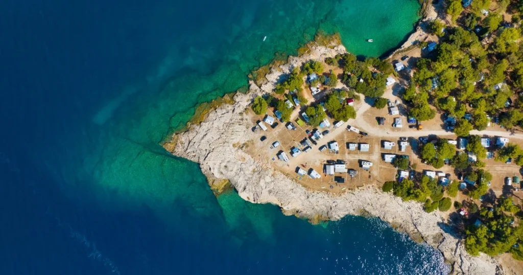 Kamp uz hrvatsku obalu snimljen iz zraka s kamp prikolicama i kristalno čistim morem.
