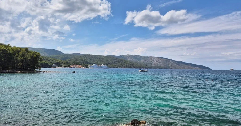 Pogled na tirkizno more i obalu Starog Grada na otoku Hvaru za sunčanog dana, s jedrilicom i trajektom u pozadini.