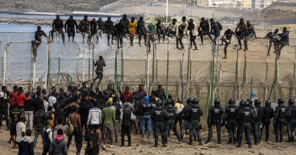 Migranti pokušavaju prijeći graničnu ogradu u španjolskoj enklavi Ceuti dok sigurnosne snage nadziru situaciju.